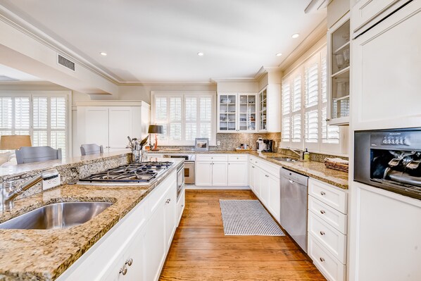 A modern kitchen with white cabinetry, granite countertops, and a wooden floor. - Beach cottage with private pool & spa, ocean views, & shared pool access (St. Simons Island)