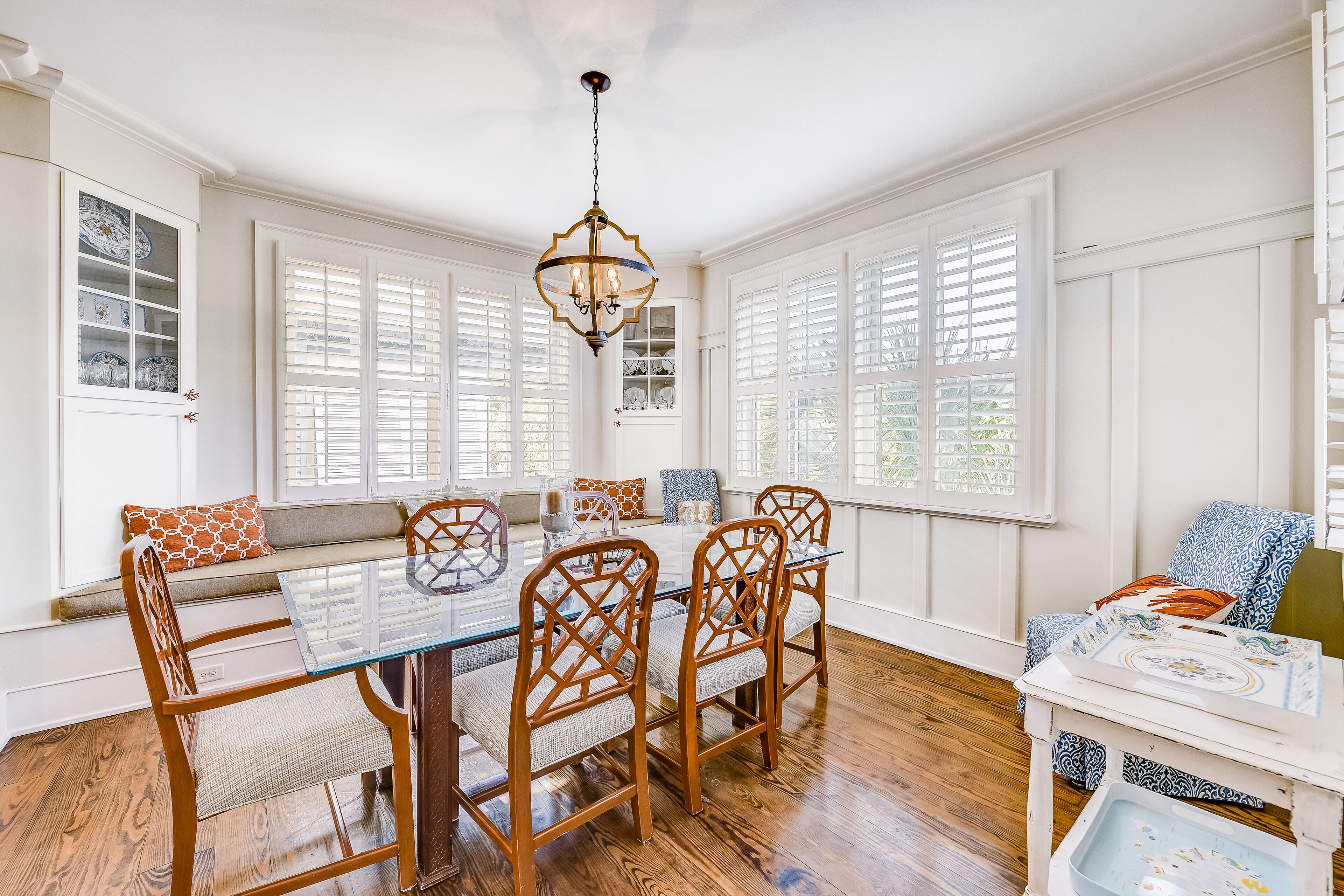 A dining area with a glass-top table, wooden chairs, and a chandelier.
