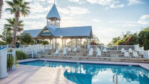 A pool area with a covered seating area, palm trees, and a building with a tower. - Charleston-style cottage w/ lovely decks, steps to the beach & pools (St. Simons Island)
