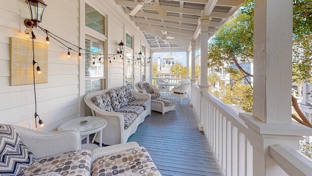 A covered porch with white railings, wicker furniture, and string lights. - Charleston-style cottage w/ lovely decks, steps to the beach & pools (St. Simons Island)
