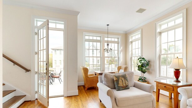 A spacious living room with hardwood floors, a white sofa, wicker chairs, and large windows. - Luxury cottage with pools & multiple decks, 1/2 block to beach (St. Simons Island)