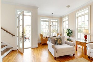 Un salon spacieux doté de planchers en bois, d’un canapé blanc, de fauteuils en osier et de grandes fenêtres.