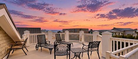 A balcony with a table and chairs, a railing, and a view of the sky.