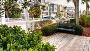 A wooden deck with a bench, surrounded by lush greenery and a white picket fence. - Luxury cottage with pools & multiple decks, 1/2 block to beach (St. Simons Island)