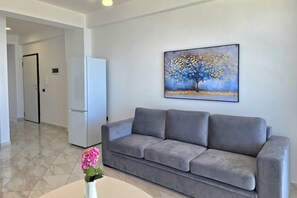 Ein modernes Wohnzimmer mit einem grauen Sofa, einem weißen Couchtisch und einem Baumgemälde an der Wand.