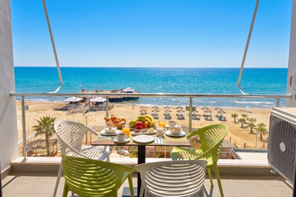 Een balkon met een ontbijttafel, uitkijkend op het strand.