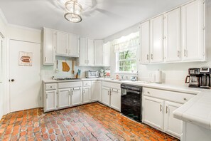 A kitchen with white cabinets, a brick floor, and a window with a view of greenery. - Relaxing, dog-friendly home with furnished patio, washer/dryer, WiFi, & AC (St. Simons Island)