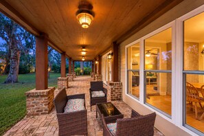 An outdoor covered patio with wicker furniture and brick accents, leading to a glass door entrance. - Dog-friendly home with central AC, washer/dryer & spacious backyard - near beach (St. Simons Island)