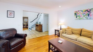 Una sala de estar con un sofá de cuero marrón, un sofá color beige, una mesa de centro de madera y un cuadro en la pared.