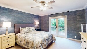 Un dormitorio con cama, mesitas de noche, ventilador de techo y puerta corrediza de vidrio a un balcón.