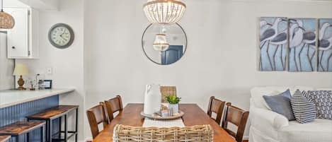 A dining area with a wooden table, chairs, a chandelier, a clock, and wall art.