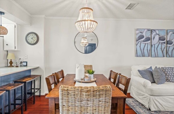 A dining area with a wooden table, chairs, a chandelier, a clock, and wall art. - Snowbird-friendly condo with patio, central AC, W/D, pool & tennis - near beach (St. Simons Island)