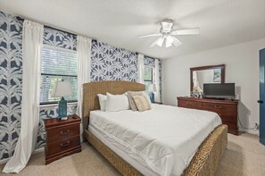 A bedroom with a bed, nightstands, a television, and a ceiling fan. - Snowbird-friendly condo with patio, central AC, W/D, pool & tennis - near beach (St. Simons Island)