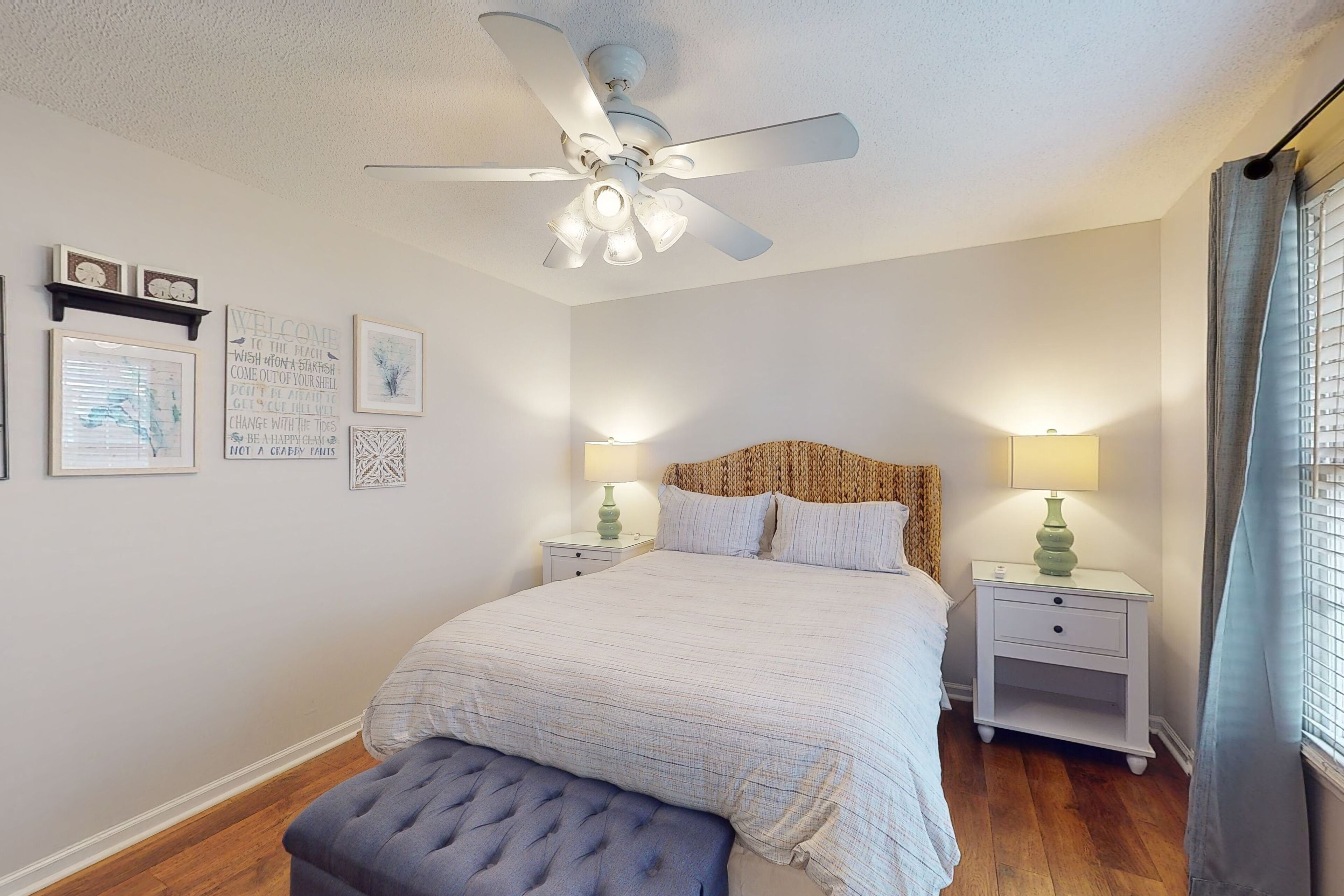 A bedroom with a bed, a ceiling fan, bedside tables with lamps, and framed artwork on the wall.