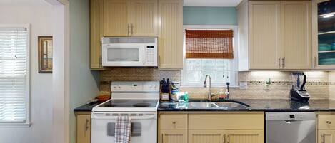 A kitchen with beige cabinets, a white stove, a microwave, a dishwasher, and a window with a brown blind.