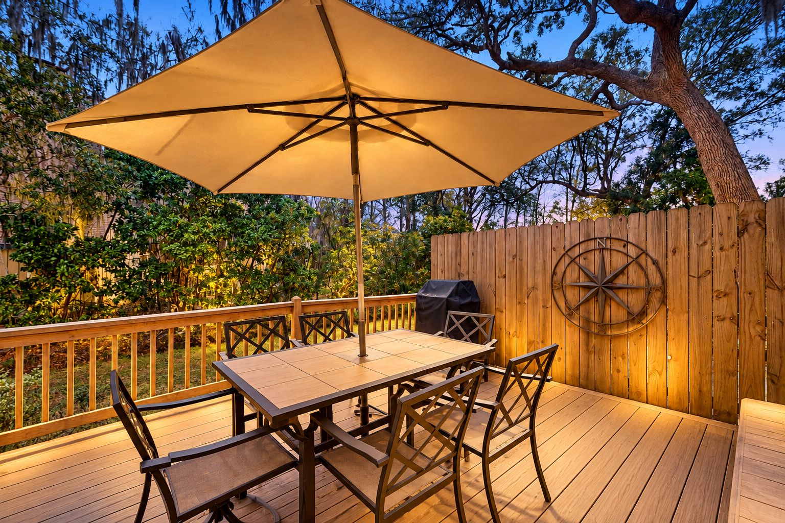 Une terrasse extérieure avec une table et des chaises, un grand parasol et une clôture en bois ornée d’une boussole.