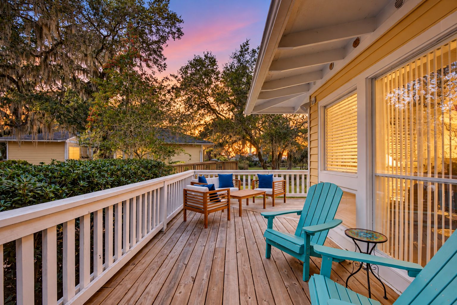 A wooden deck with outdoor furniture, a railing, and a view of the surrounding trees and houses.