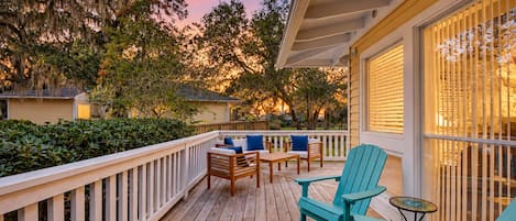 A wooden deck with outdoor furniture, a railing, and a view of the surrounding trees and houses.