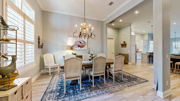 A spacious dining area with a chandelier, white chairs, and a blue patterned rug. - Golf course-view home near beaches with deck, porch, grill, streaming, W/D, & AC (St. Simons Island)