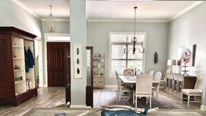 A spacious dining area with a long table, chairs, and a chandelier. - Golf course-view home near beaches with deck, porch, grill, streaming, W/D, & AC (St. Simons Island)