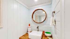 Une salle de bain avec un meuble-lavabo en bois, un lavabo blanc et un miroir rond.