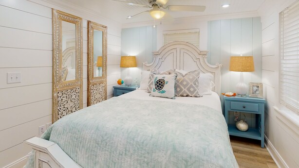 Une chambre à coucher comprenant un lit, deux tables de chevet, un ventilateur de plafond et des lampes décoratives.