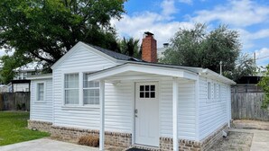 Une petite maison de plain-pied, à l’extérieur blanc, avec une cheminée en briques et une porte d’entrée dotée d’une petite fenêtre.