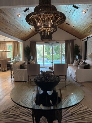 A spacious living room with a round glass table, two sofas, a chandelier, and a view of the outdoors. - Lakefront home with private pool & outdoor space for entertaining (St. Simons Island)