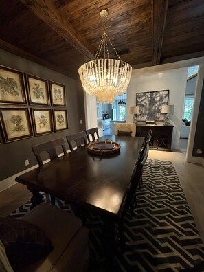 A dining room with a large wooden table, framed botanical prints on the wall, and a hanging chandelier. - Lakefront home with private pool & outdoor space for entertaining (St. Simons Island)
