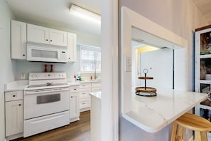 A modern kitchen with white cabinetry, a built-in microwave, a stove, and a marble countertop. - Private retreat with access to community pool & nearby entertainment (St. Simons Island)