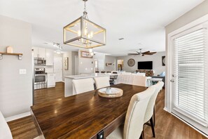 A spacious kitchen with modern appliances, a dining area with a wooden table, and a ceiling fan. - Private Pool, LSV/Golf Cart, Bikes, & 2 Kitchens! Easy Walk to Beach! Pet Friendly (Santa Rosa Beach)