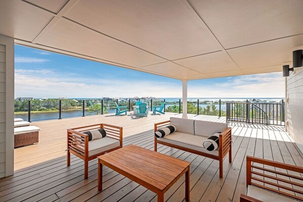 A covered outdoor deck with wooden furniture, a view of a body of water, and a railing.