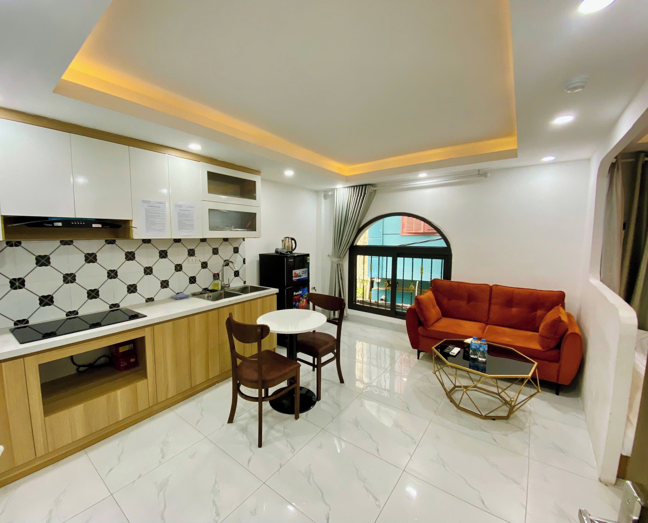 A modern kitchen with a dining area, a sofa, and a view through a window.