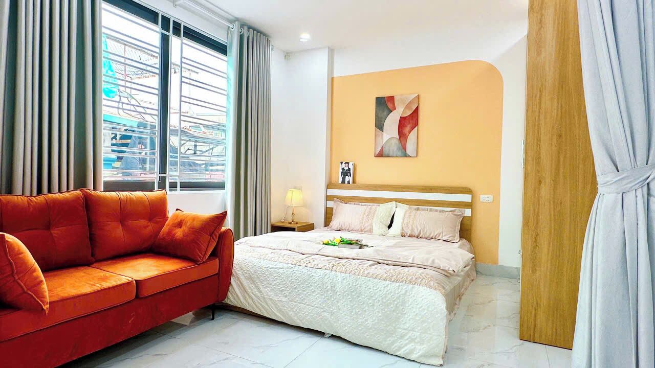 A hotel room with a bed, a red sofa, a nightstand, and a wall with a picture.