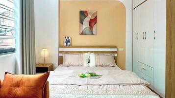 A modern hotel room with a large bed, a sofa, a nightstand, a lamp, a wardrobe, and a window with curtains.