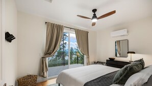 Une chambre à coucher comprenant un lit, un ventilateur de plafond, une fenêtre avec des rideaux, une table de chevet, une lampe et une vue sur l’extérieur.