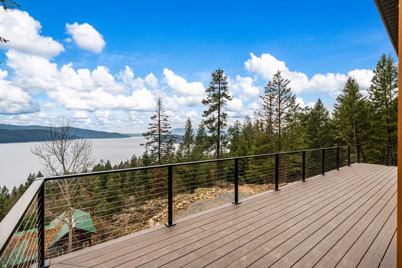 Une terrasse en bois avec une rambarde en métal, donnant sur un lac et une forêt.