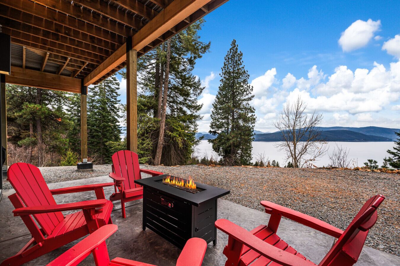Un espace extérieur aménagé avec des sièges, abrité par un toit, comprenant des fauteuils Adirondack rouges et un foyer noir.