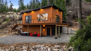 Une cabane en rondins à deux étages, dotée d’un balcon, d’un jacuzzi et de chaises rouges à l’extérieur.