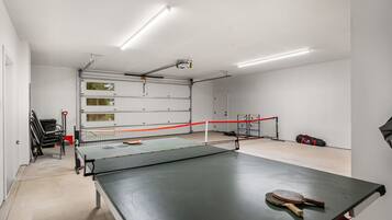 Une table de ping-pong avec un filet, dans une pièce aux murs blancs et dotée d’une porte de garage.
