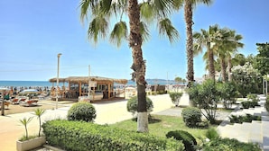 A beachside resort with palm trees, a thatched-roof building, and a clear view of the sea. - Merville Happy Stay 083, Durres, Albania (Durres)