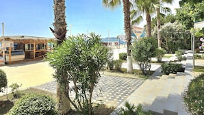 A hotel with a thatched-roof building, palm trees, and a paved walkway. - Merville Happy Stay 083, Durres, Albania (Durres)