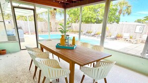 A covered patio with a wooden table and white plastic chairs, overlooking a swimming pool and a wooden fence. - Palm Villa - 4 Bed, 2.5 Bath, Heated Pool, Hot Tub, Blocks to Beach, Sleeps 10+ (Satellite Beach)