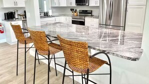 A modern kitchen with white cabinets, stainless steel appliances, and a marble countertop. - Palm Villa - 4 Bed, 2.5 Bath, Heated Pool, Hot Tub, Blocks to Beach, Sleeps 10+ (Satellite Beach)