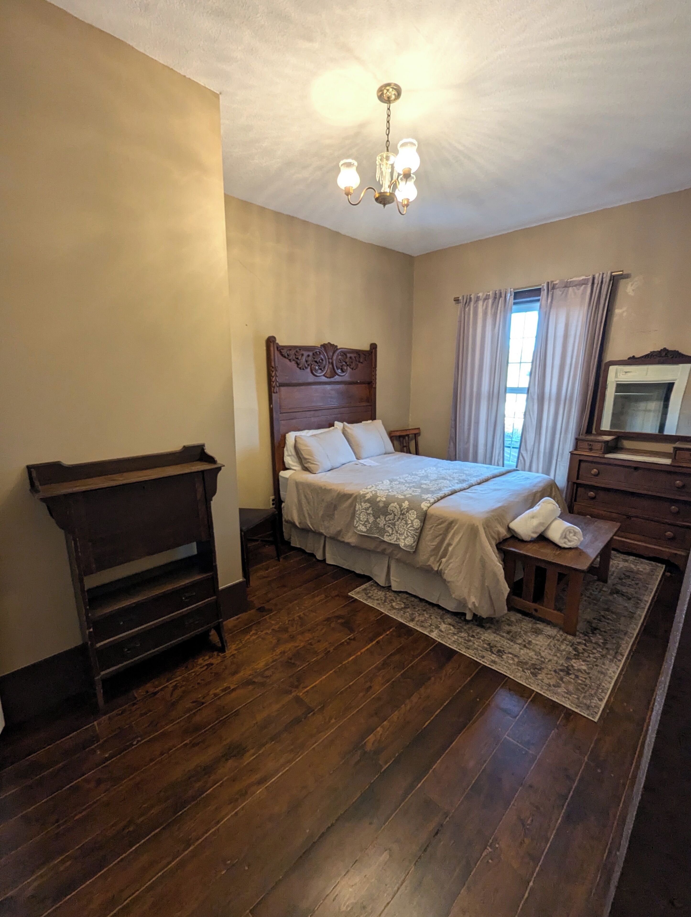 A bedroom with a wooden bed, a nightstand, a dresser, and a chandelier.