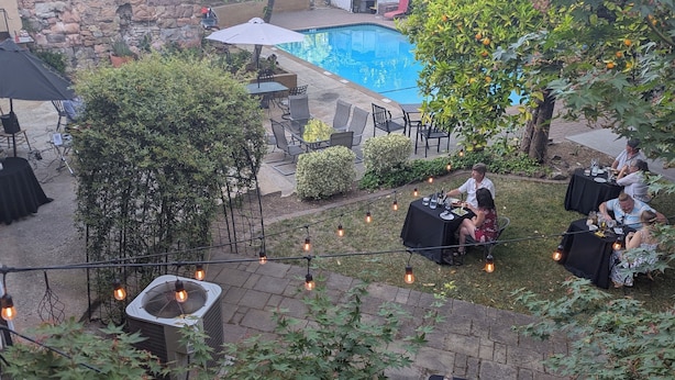 Un patio trasero con muro de piedra, piscina, mobiliario exterior e iluminación con guirnaldas.