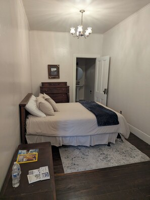 A bedroom with a bed, dresser, nightstand, and a chandelier. - Hotel Leger (Mokelumne Hill)