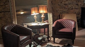 Una habitación con pared de piedra, un espejo grande, dos sillones de cuero, una mesa con lámpara y una alfombra de piel de vaca.