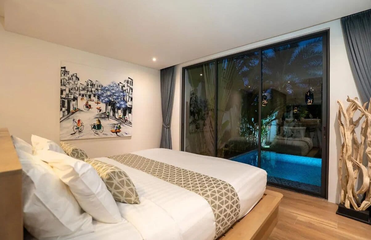 A bedroom with a large bed, a painting on the wall, and a sliding glass door leading to a pool area.