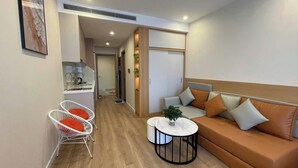 A modern living room with a sofa, two white chairs with orange cushions, a round coffee table, and a plant. - Icon 40 Villa (Bai Chay)